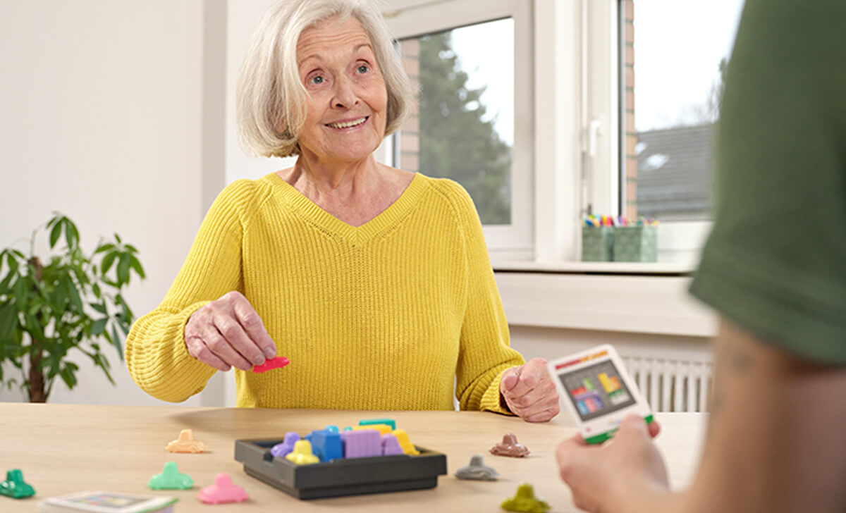 Seniorin bei einer kognitiven Therapieübung mit Spielmaterial zur Förderung der Feinmotorik und des Gedächtnisses
